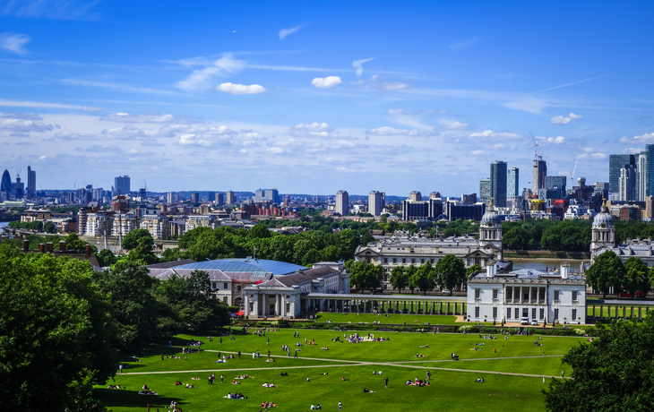 Wiese mit Menschen, historische Gebäude, Londoner Skyline im Hintergrund, blauer Himmel.