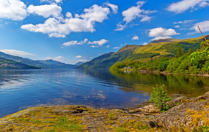 Landschaft mit See, Hügeln und blauem Himmel mit Wolken.