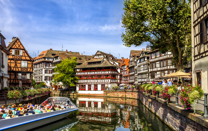 Historische Fachwerkhäuser am Fluss mit touristenbefahrener Bootsfahrt.