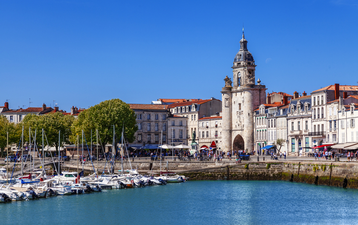 Hafen mit Segelbooten und historischer Turm in einer europäischen Stadt.