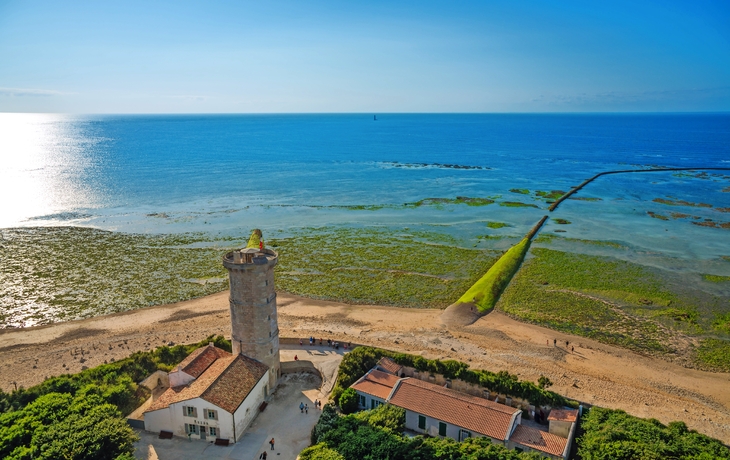 Leuchtturm an einer Küste mit Meer bei Sonnenschein und klarem Himmel.