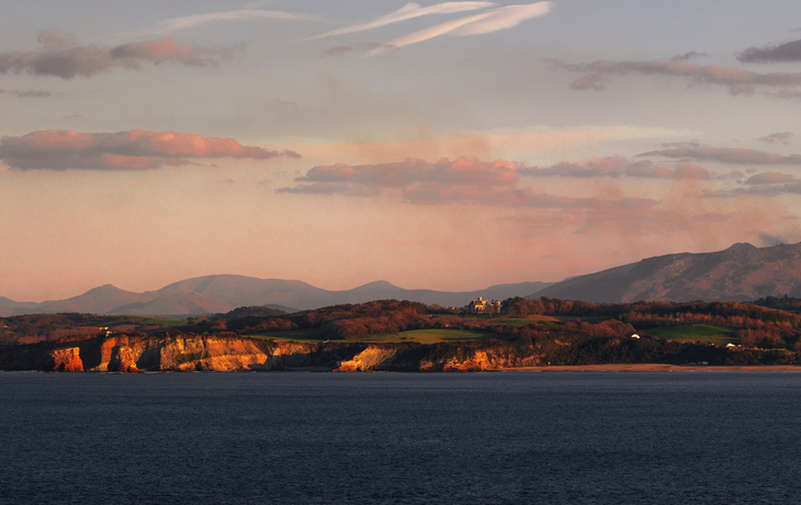 Küste mit Bergen im Hintergrund bei Sonnenuntergang.