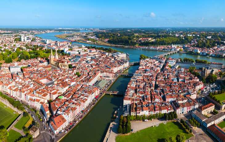Luftaufnahme einer Stadt mit Fluss und Brücken im Sonnenschein.