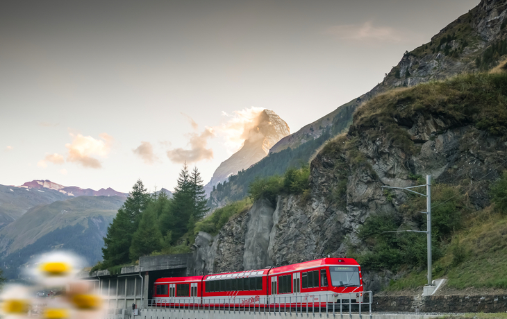 Roter Zug fährt vor Bergkulisse entlang, Matterhorn im Hintergrund.
