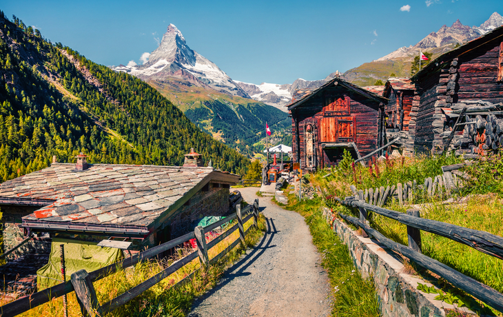 Alpenlandschaft mit Holzhütten und dem Matterhorn im Hintergrund bei sonnigem Wetter.