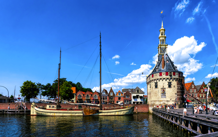 Mittelalterlicher Turm und Segelboot am Wasser mit Stadt im Hintergrund.