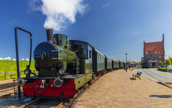 Historische Dampflokomotive auf Bahngleis vor blauem Himmel und Backsteingebäuden