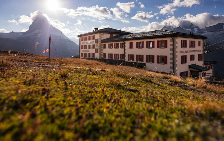 Hotel am Hang mit Bergen im Hintergrund und Sonnenschein.