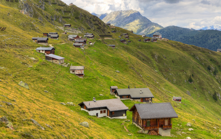Alpenhütten auf grünen Berghängen bei bewölktem Himmel.
