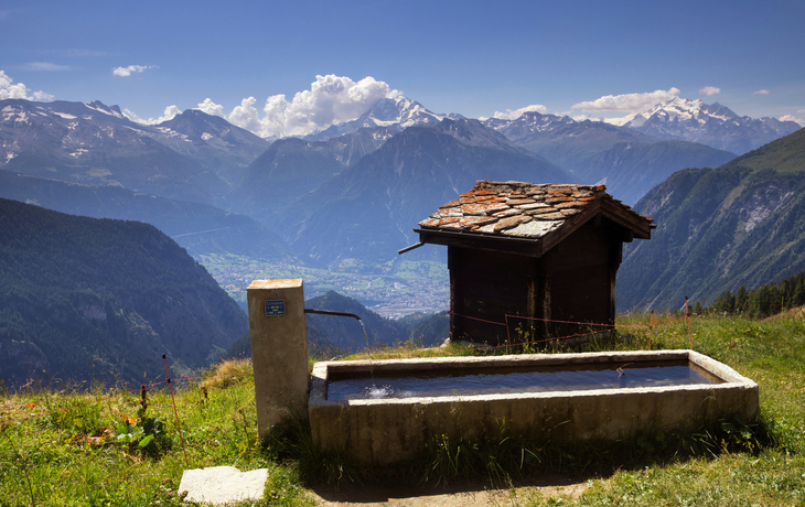 Almhütte mit Brunnen in alpiner Berglandschaft.