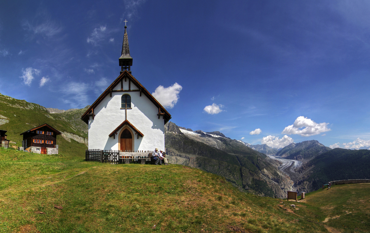 Bergkapelle neben Holzhäusern mit Alpenpanorama im Hintergrund