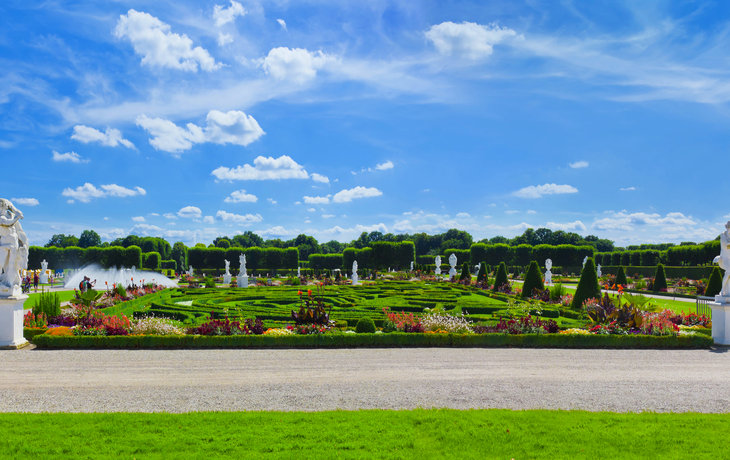 Barockgarten mit bunten Blumen, Statuen und blauem Himmel im Hintergrund.
