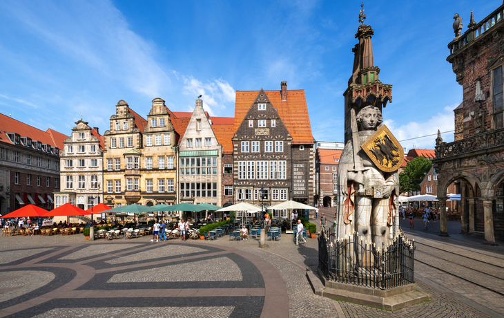Historischer Platz mit Roland-Statue und Fachwerkhäusern bei sonnigem Wetter.