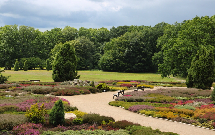 Gartenlandschaft mit Blumenbeeten, Bäumen und Wolken am Himmel