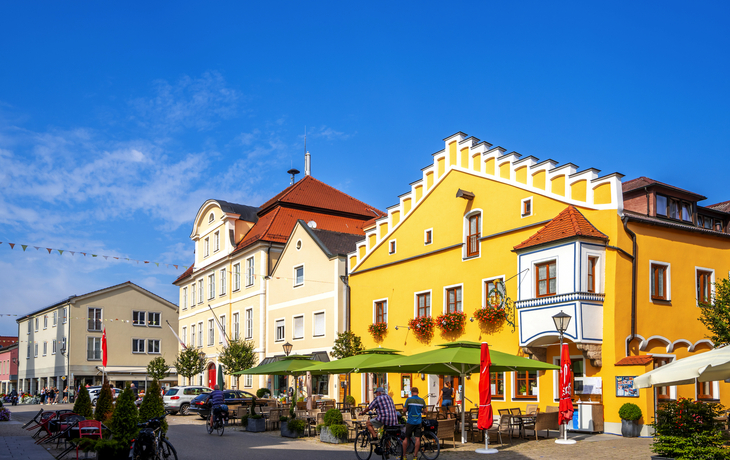 Farbige Häuser und Menschen auf einem sonnigen Platz in einer europäischen Stadt.