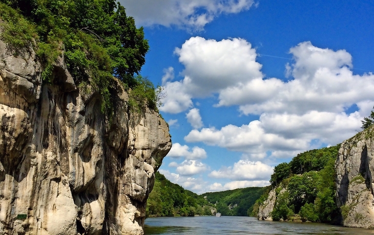 Fluss zwischen hohen Felsklippen mit blauem Himmel und Wolken.