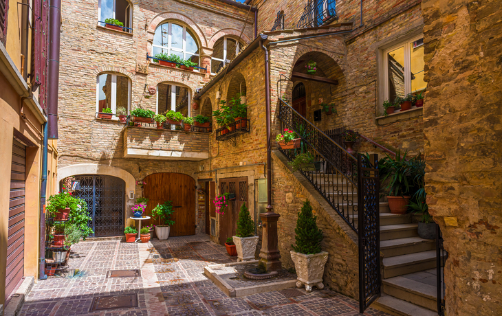 Stein-Innenhof mit Treppen und Pflanzen in Töpfen bei Sonnenschein.