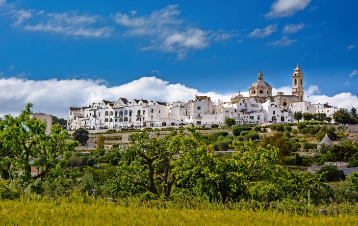 Stadtansicht mit weißen Gebäuden und einer Kirche unter blauem Himmel.