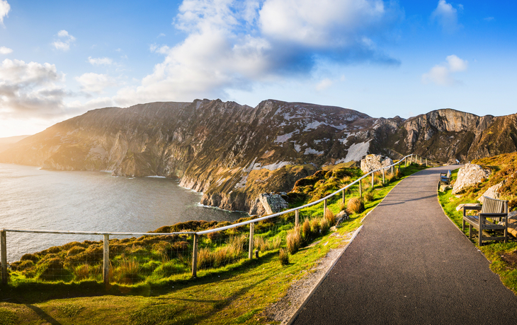 Klippenlandschaft mit Küstenweg und Meer bei Sonnenuntergang.