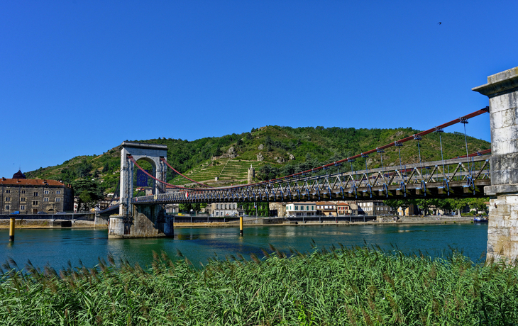 Hängebrücke über einen Fluss mit Hügel im Hintergrund.