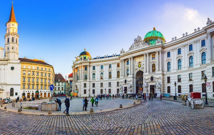Historisches Gebäude und Kirche mit gepflastertem Platz und Menschen.