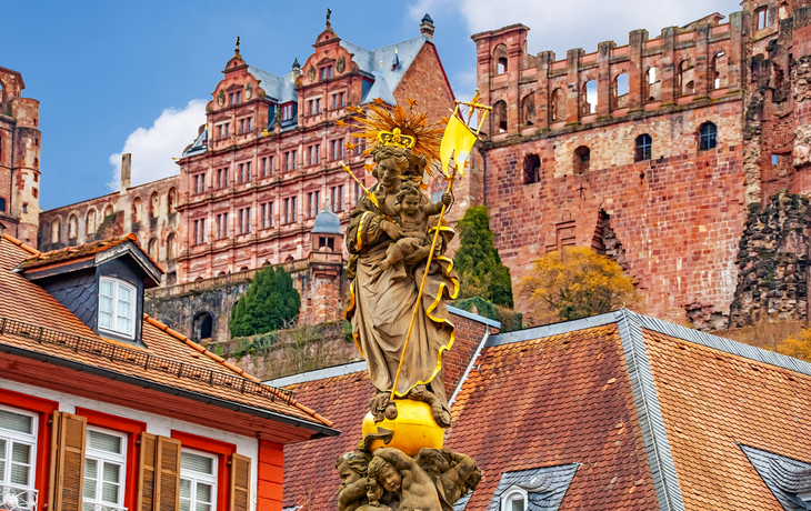 Historisches Schloss vor Wohngebäuden, mit denkmalgeschützter Statue im Vordergrund.
