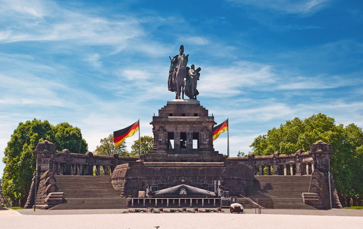 Denkmal mit Reiterstatue, deutscher Fahne und blauem Himmel im Hintergrund.