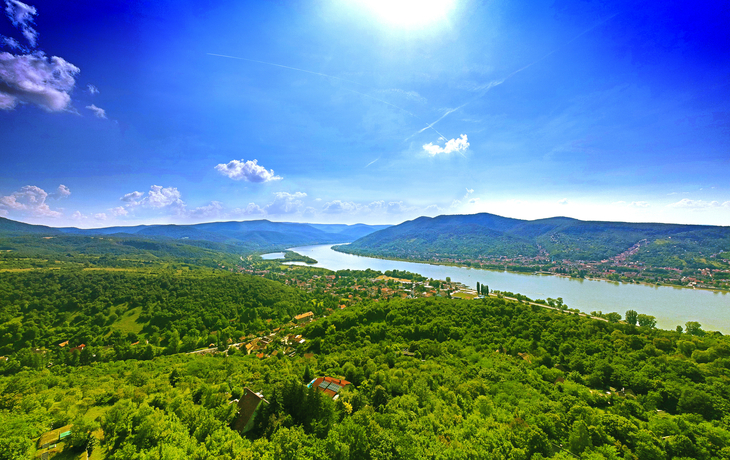 Luftaufnahme eines Flusses mit bewaldeten Hügeln und blauem Himmel.