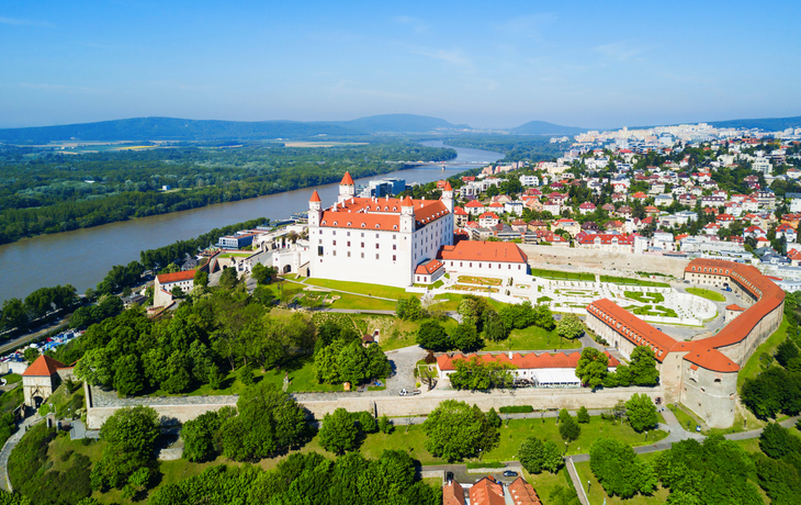 Luftaufnahme einer Burg mit rotem Dach in einer grünen Landschaft an einem Flussufer.