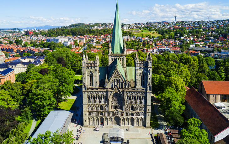 Luftaufnahme einer Kathedrale in einer Stadtlandschaft mit grünem Turm und vielen Bäumen.
