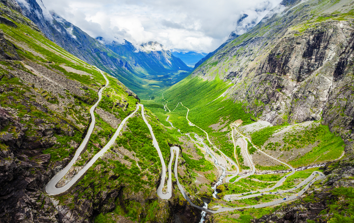 Serpentinenstraße durch grünes Tal und steile Berge.