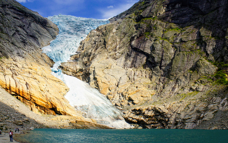 Gletscher zwischen hohen Felswänden über einem türkisfarbenen See bei sonnigem Wetter.