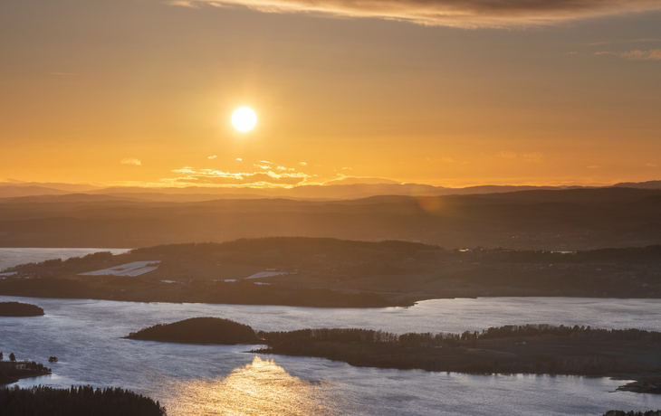 Sonnenuntergang über einem See mit bewaldeten Inseln und bewölktem Himmel.