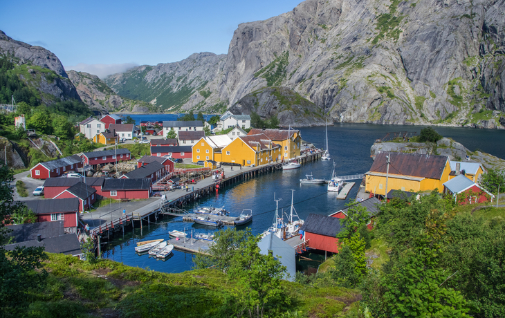 Bunte Holzhäuser in einem norwegischen Fischerdorf am Wasser, umgeben von Bergen.