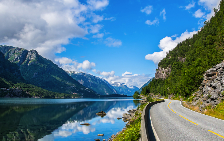 Straße entlang eines Fjords in Norwegen mit Bergen und blauen Himmel.