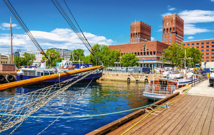 Segelschiff im Hafen mit roten Backsteingebäuden im Hintergrund an einem sonnigen Tag.