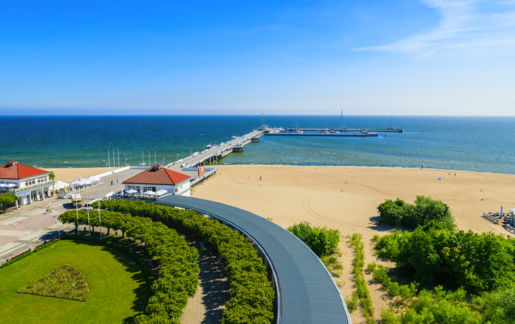 Strandpromenade mit Sandstrand und Steg am Meer bei klarem Himmel.