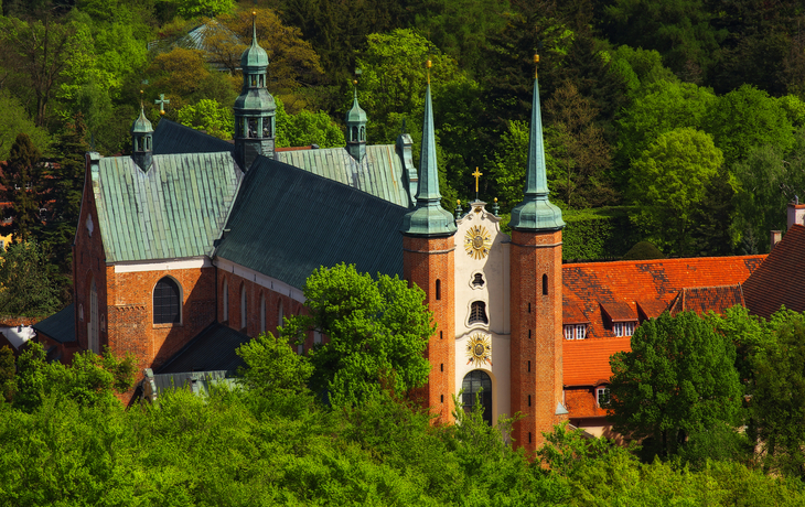 Kirche mit grünen Dächern, umgeben von Bäumen und bewaldeter Landschaft.