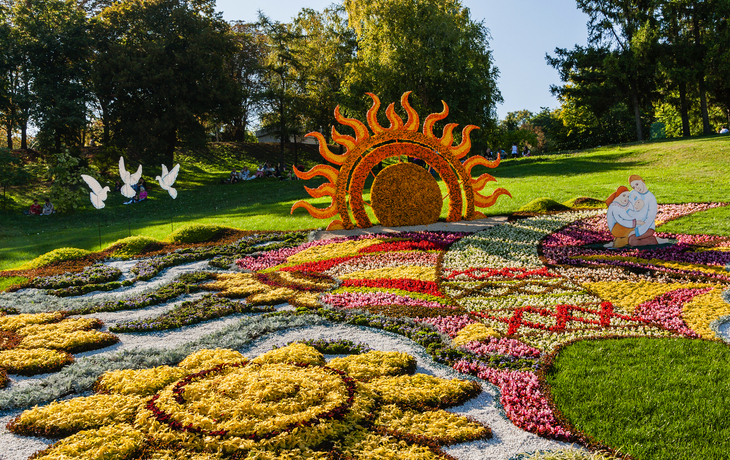 Ein bunter Blumengarten mit Sonne und Figuren in einem Park.