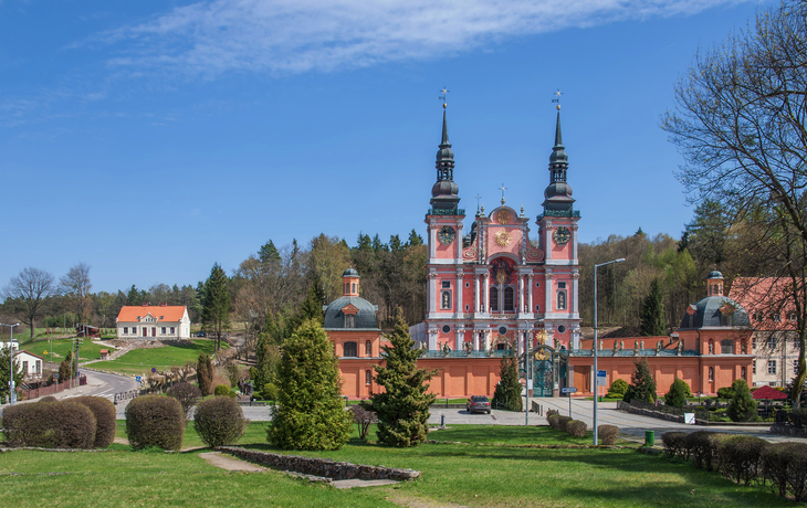 Kirche mit Türmen in grüner, ländlicher Landschaft bei blauem Himmel.