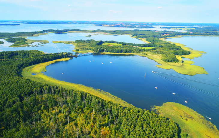 Luftaufnahme von Seenlandschaft mit grüner Vegetation und Booten auf dem Wasser.