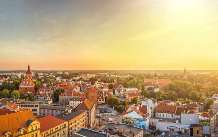 Panorama einer Stadtlandschaft bei Sonnenuntergang mit roten Dächern und Kirche.