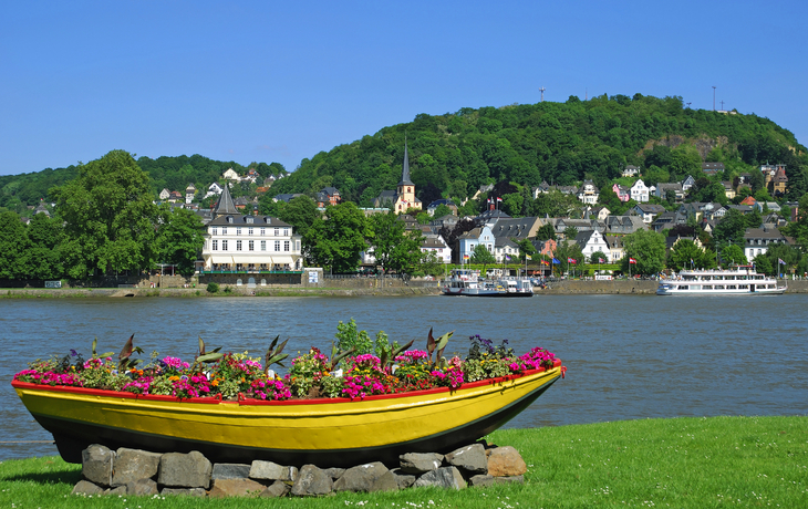 Gelbes Blumenboot vor Fluss und grüner Hügelkette mit Stadt im Hintergrund.