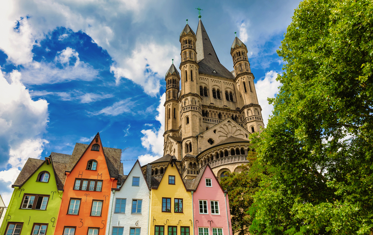 Bunte Häuser vor Kirche mit Türmen und blauem Himmel in Köln, Deutschland