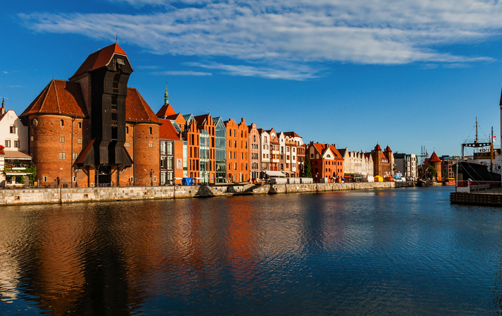 Häuserreihe an einem Fluss mit blauem Himmel und Wolken im Hintergrund.