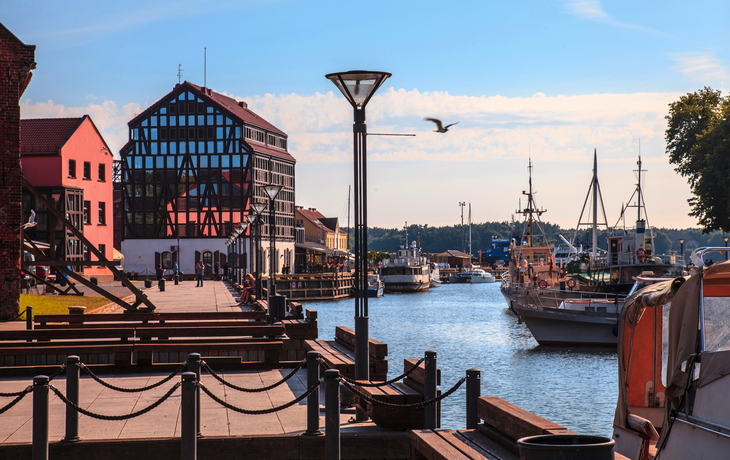 Hafen mit modernen Gebäuden und mehreren am Dock anliegenden Booten bei sonnigem Wetter.