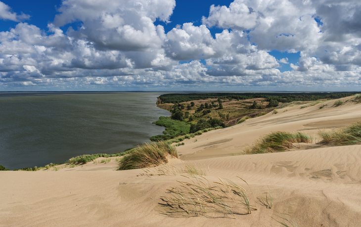 Küstenlandschaft mit Sanddünen und bewölktem Himmel am Meer.