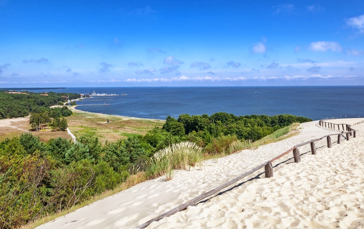 Dünenlandschaft mit Blick auf das Meer und bewaldete Küstenlinie.