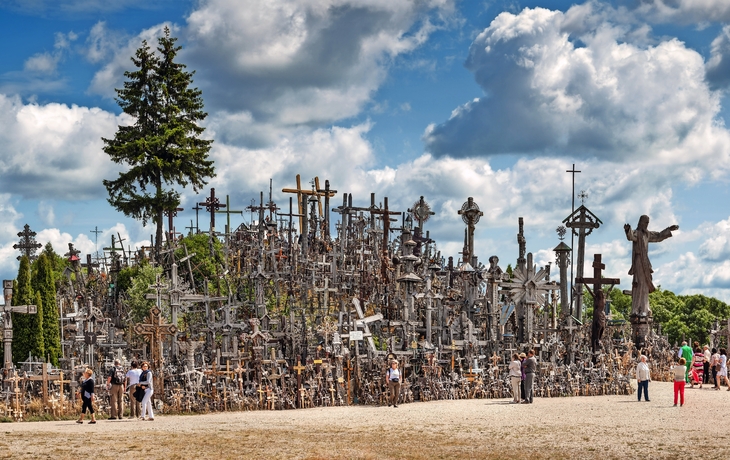 Hügel mit zahlreichen Kreuzen unter bewölktem Himmel, Menschen besichtigen die Stätte.