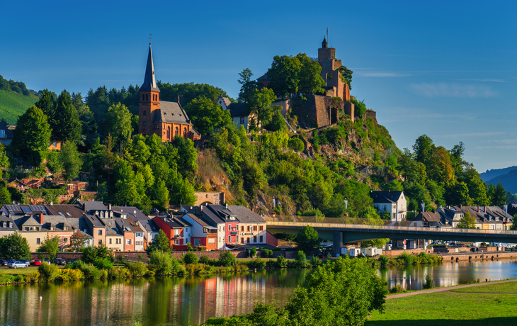 Burg und Kirche auf einem Hügel über einem Fluss mit Brücke und Häusern.